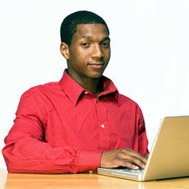 A person sitting at a desk using a laptop, wearing a red shirt, and displaying a confident expression.