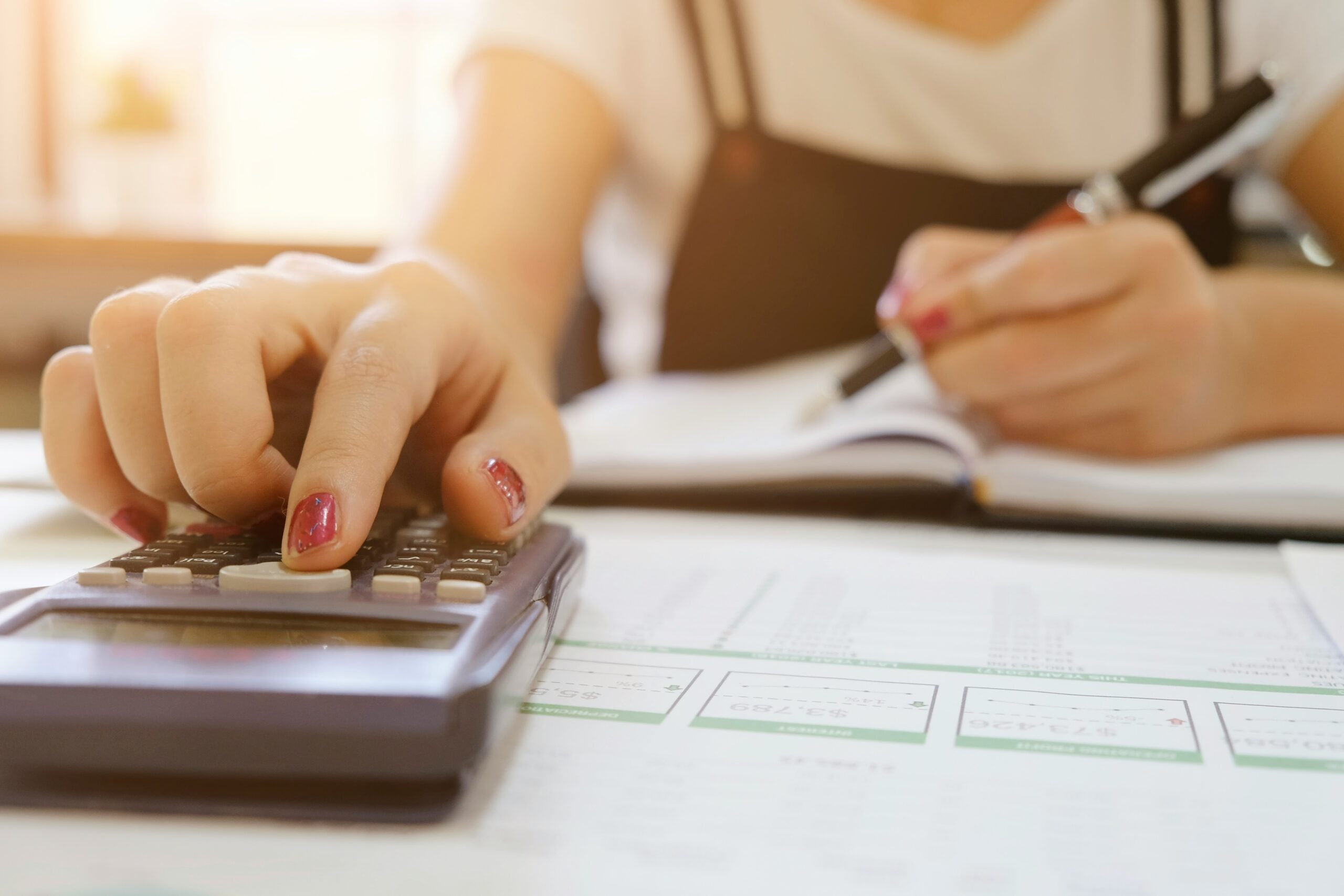 A person using a calculator while writing in a notebook, representing financial calculations or budgeting.