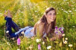 A person is lying in a field of wildflowers, holding a bouquet and smiling. Sunlight illuminates the scene, suggesting a sense of joy and tranquility.