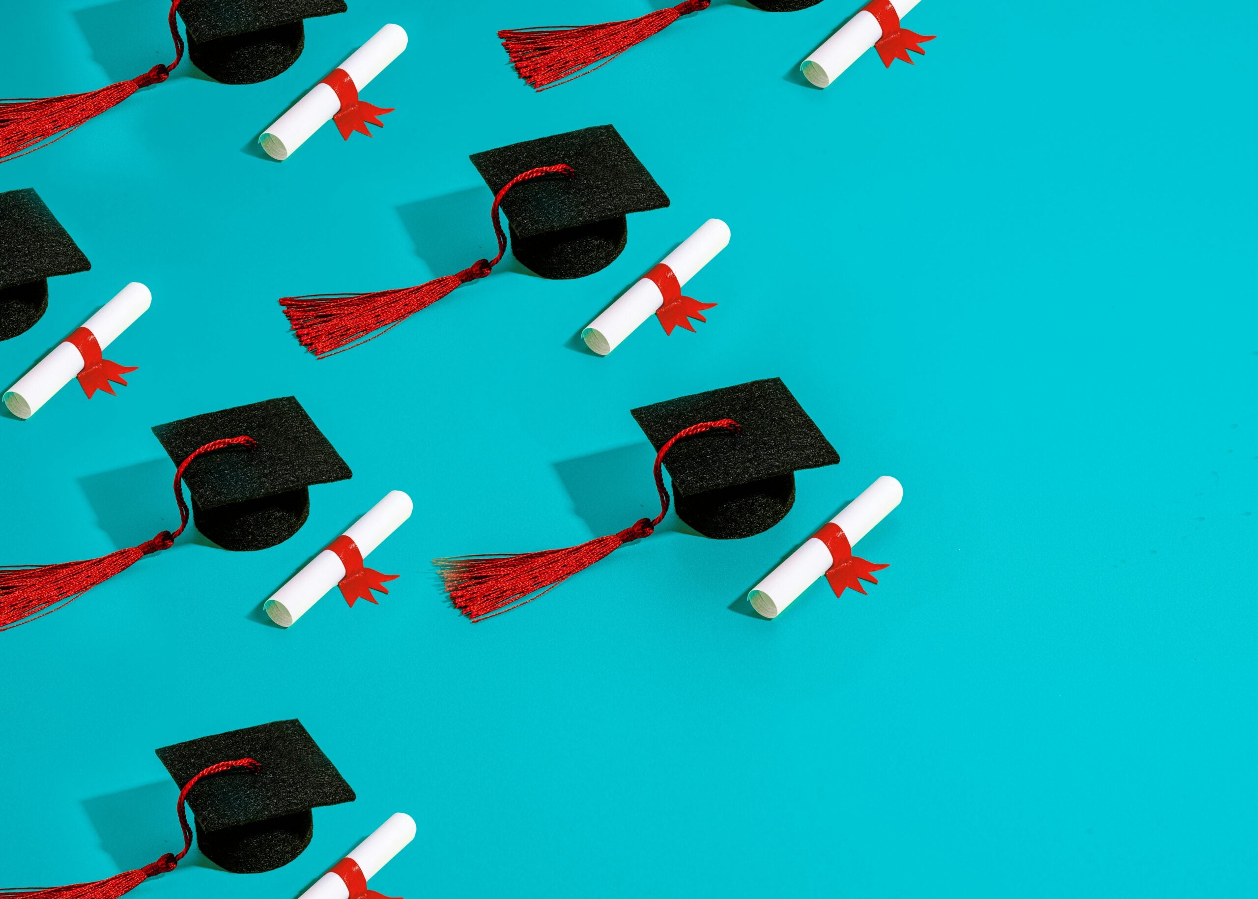 Graduation caps and diplomas with red tassels and ribbons on a blue background, representing academic achievement.