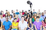 A diverse group of people sitting together, facing forward, with a microphone on a stand positioned in front of them.
