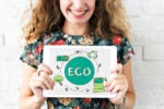 Person holding a tablet displaying eco-friendly symbols, including a recycling sign, battery icon, and the word "ECO," promoting sustainability.