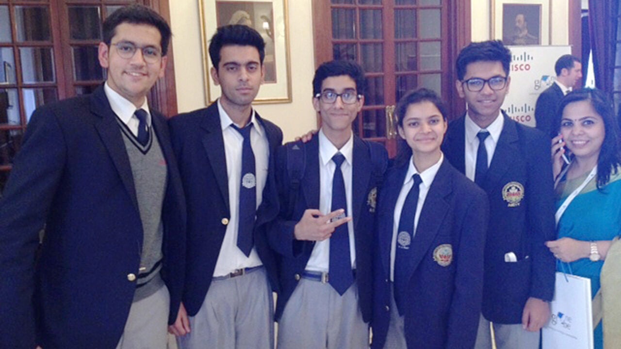 A group of six people wearing formal attire, including blazers with badges, posing together indoors.