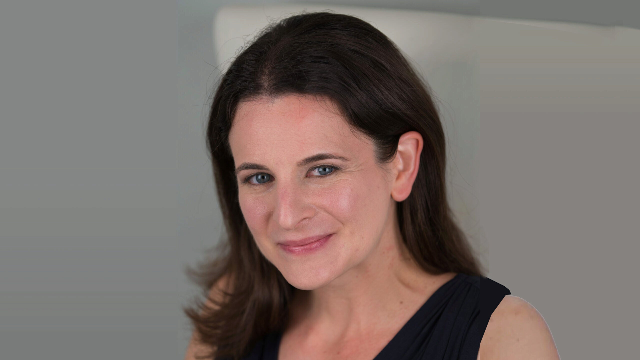 Headshot of a person with long dark hair and a slight smile against a neutral background.