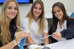 Three people sitting at a table, smiling, and holding droppers over a science experiment. They are in a classroom setting.
