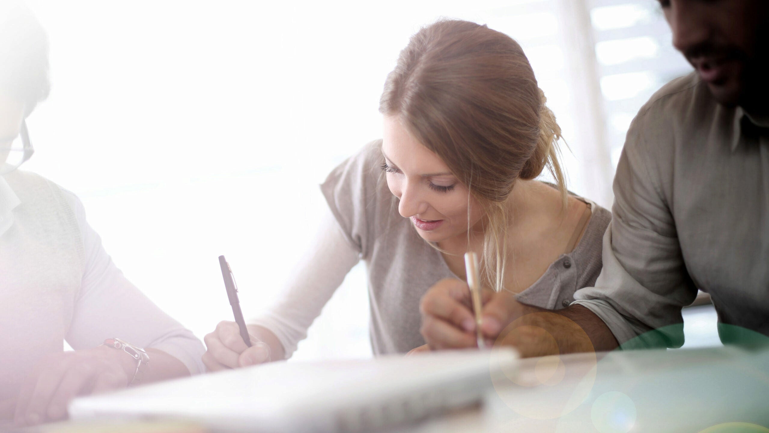 People sitting together and writing, likely in a collaborative or educational setting. The image suggests teamwork or study.