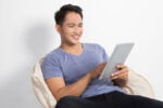 A person is sitting comfortably on a bean bag, smiling, and using a tablet device.