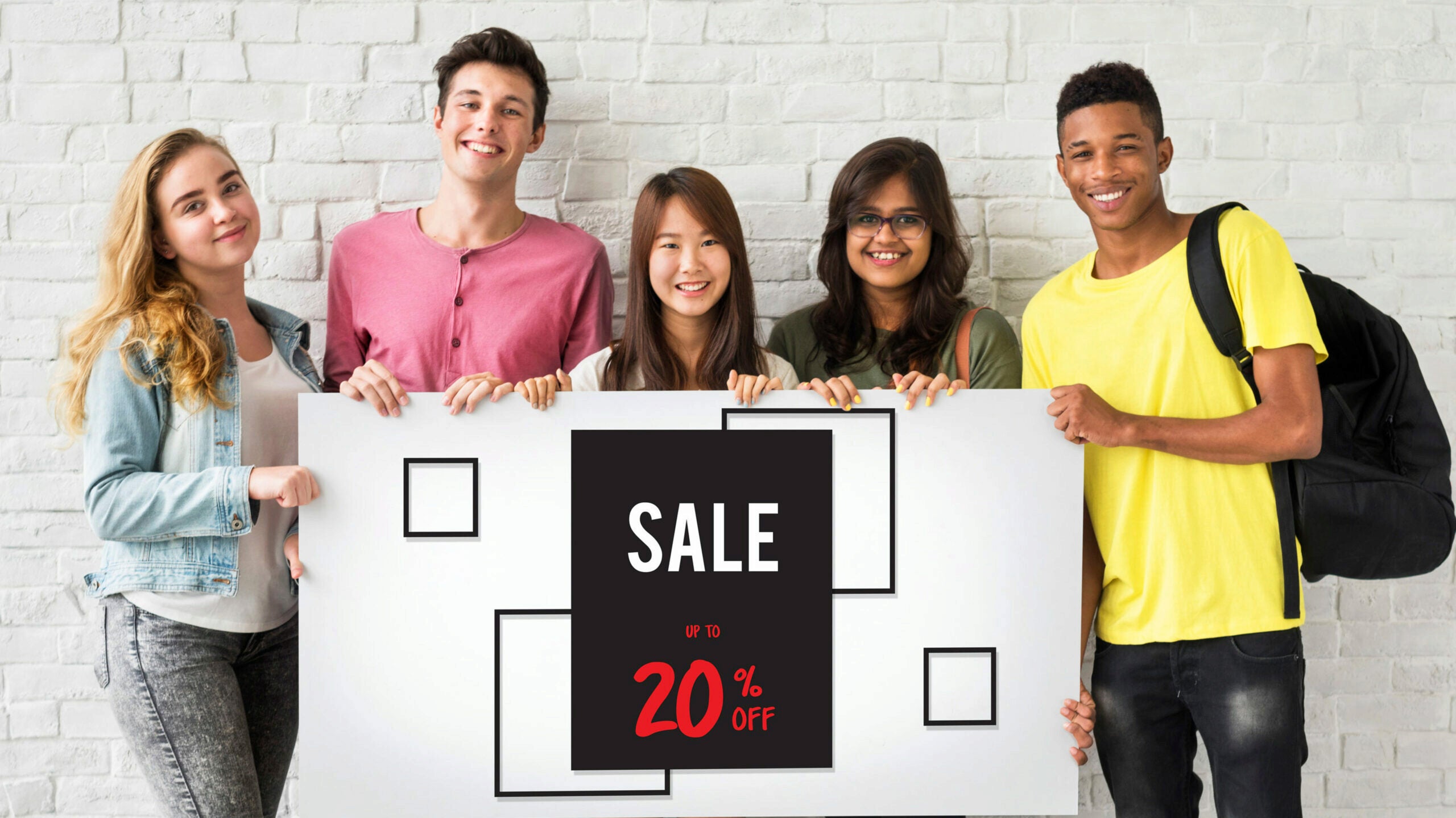 Five people smiling and holding a sign that says "SALE UP TO 20% OFF" against a white brick wall.