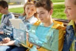 Three young people sitting on a bench looking at a tablet, with digital data visuals and graphs overlayed, symbolizing technology and learning.