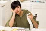 A person sitting at a table, looking concerned while holding a receipt from a calculator. They appear to be working on financial calculations.