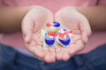 Hands holding four colorful laundry detergent pods with red, blue, and white swirls.