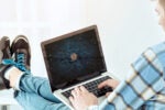A person in casual attire is using a laptop displaying a digital circuit board with the Bitcoin logo. The scene suggests a focus on cryptocurrency.