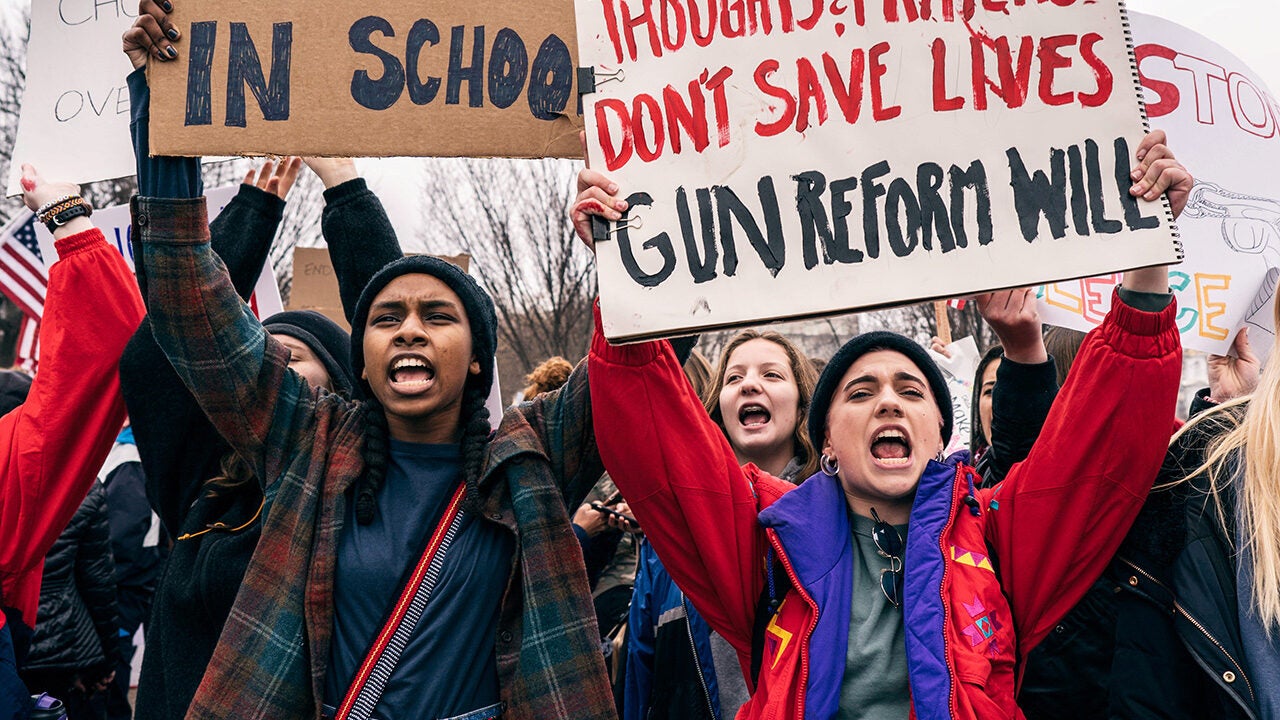 Protesters holding signs advocating for gun reform and safety in schools, with expressions of determination and advocacy.