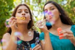 Two individuals blowing bubbles outdoors, surrounded by greenery, capturing a playful and carefree moment.
