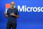 A person speaking on stage with a Microsoft logo in the background.