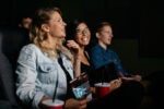 People enjoying a movie in a theater, smiling and holding snacks and drinks.