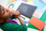 A person sitting at a desk with a graphic tablet and colorful swatches, possibly engaged in graphic design or digital art.