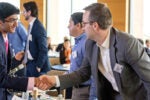 People in business attire shaking hands in a conference setting, representing networking or professional agreement.
