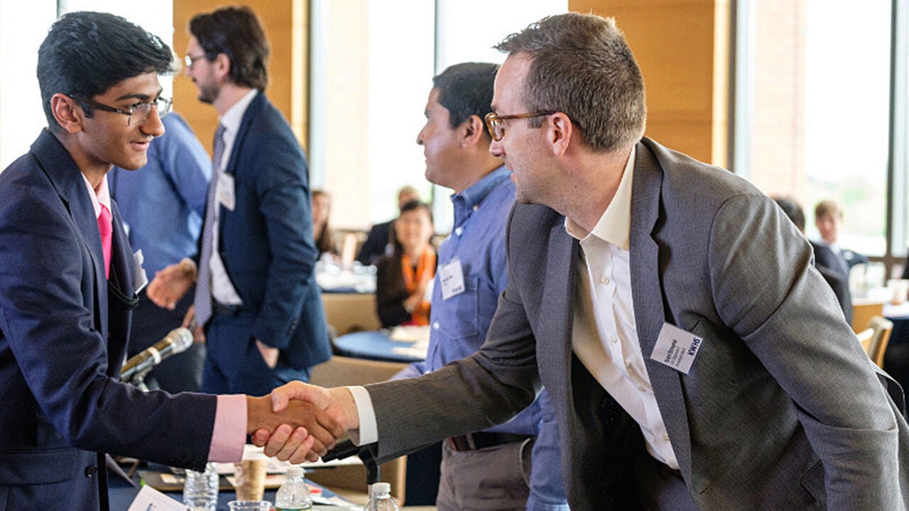 People in business attire shaking hands in a conference setting, representing networking or professional agreement.