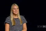 A person with long blonde hair wearing a black and white striped shirt against a black background, with the letters "KWHS" in the corner.