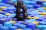 A black Bitcoin symbol surrounded by blue and yellow 3D cubes, representing digital currency and blockchain technology.