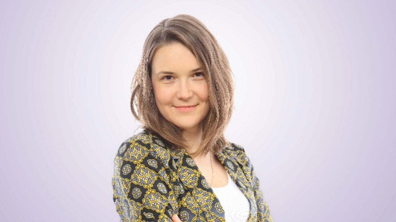 Headshot of a person with shoulder-length hair and a patterned shirt, smiling against a light background.