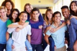 A group of smiling teenagers in a school hallway, with some giving others piggyback rides, symbolizing friendship and camaraderie.