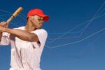 A baseball player in a red cap and striped jersey holds a bat, poised to swing. Graph lines are overlaid on the blue background.