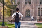 A person with a backpack stands facing a large stone building with an arched entrance, trees, and benches in the foreground, representing a university campus.