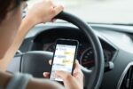 A person is texting on a smartphone while driving, showing a conversation on the screen. This represents distracted driving.