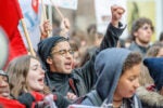 A diverse group of people participating in a protest or rally, with one person raising a fist and others holding signs.