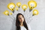 A person smiling with illustrations of glowing light bulbs around their head, symbolizing creativity and ideas.