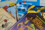 A collection of vintage tabletop role-playing game books and manuals, including "Monster Manual," "Fiend Folio," and "Deities & Demigods," with polyhedral dice and game maps.