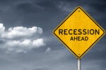 A yellow caution sign with the words "Recession Ahead" against a cloudy sky, symbolizing economic downturn.