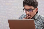 A person looking surprised while using a laptop, with a background showing blurred lines of computer code.