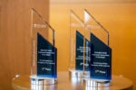 Three clear, triangular awards on a table. They are inscribed with "2018-2019 KWHS Investment Competition Global Finale, The Wharton School, University of Pennsylvania" indicating 1st and 2nd places.