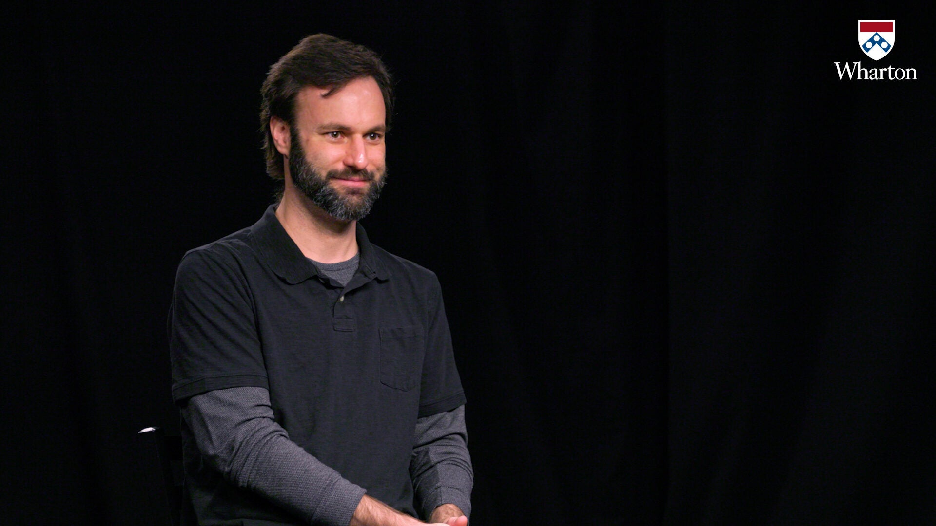 A person with a beard, wearing a dark shirt, sits against a black background with a Wharton logo in the top right corner.