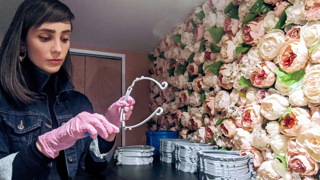 A person wearing pink gloves is examining a wire metal piece near a wall decorated with pink and white artificial roses.