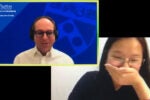 Two individuals in a virtual meeting. One is in front of a screen displaying "Wharton Global Youth Program" and appears to be speaking. The other person is smiling with a hand over their mouth.