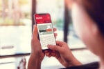 Person holding a smartphone displaying a news article about GameStop, with the logo and an upward arrow, suggesting positive news or stock trends.