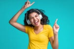 A person wearing headphones dancing joyfully, with eyes closed and fingers pointing upwards, expressing enjoyment.