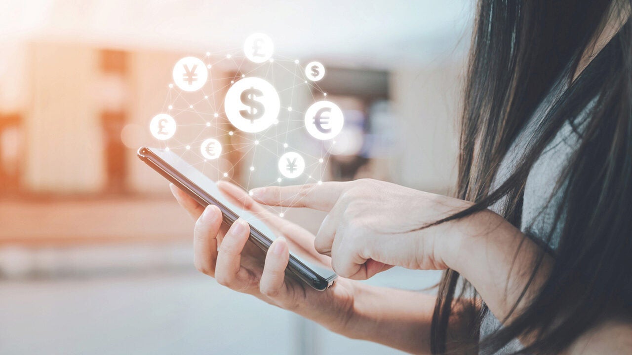 A person using a smartphone with digital currency symbols like dollar, euro, yen, and pound hovering above, representing online or mobile banking.