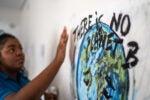 A person touches a mural featuring a depiction of Earth with the text "There is no planet B," emphasizing environmental conservation.