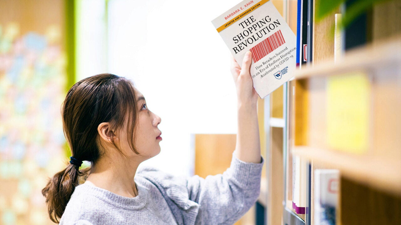 A person reaching for a book titled "The Shopping Revolution" on a bookshelf. The setting suggests a library or bookstore.