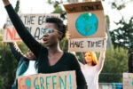 People participating in a climate protest, holding signs with messages like "Go Green" and "We Don't Have Time" to raise awareness about environmental issues.