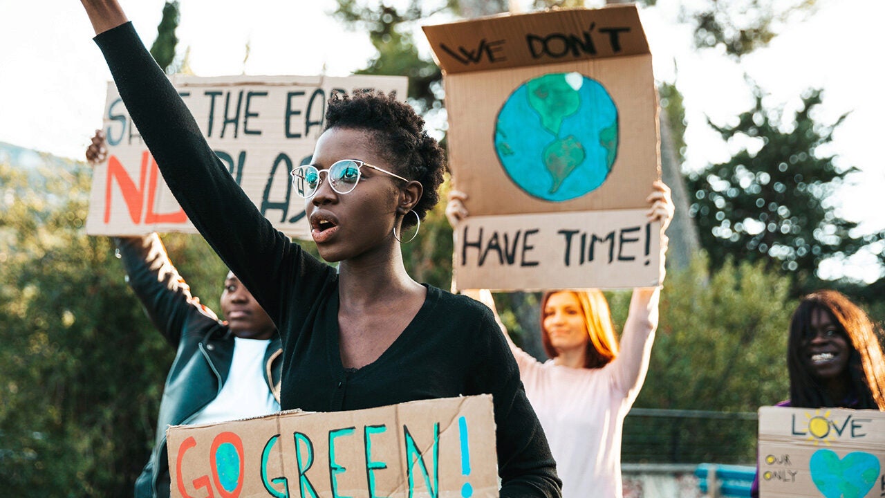 People participating in a climate protest, holding signs with messages like "Go Green" and "We Don't Have Time" to raise awareness about environmental issues.