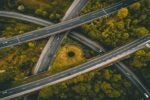 Aerial view of intersecting highways surrounded by green foliage, showcasing multiple overpasses and vehicles traveling on the roads.