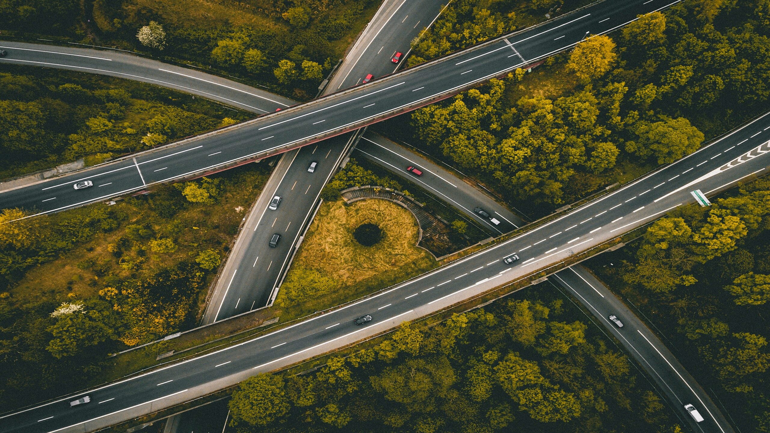 Aerial view of intersecting highways surrounded by green foliage, showcasing multiple overpasses and vehicles traveling on the roads.