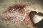 A heart-shaped cookie cutter next to a heart shape outlined in cocoa powder on a surface.