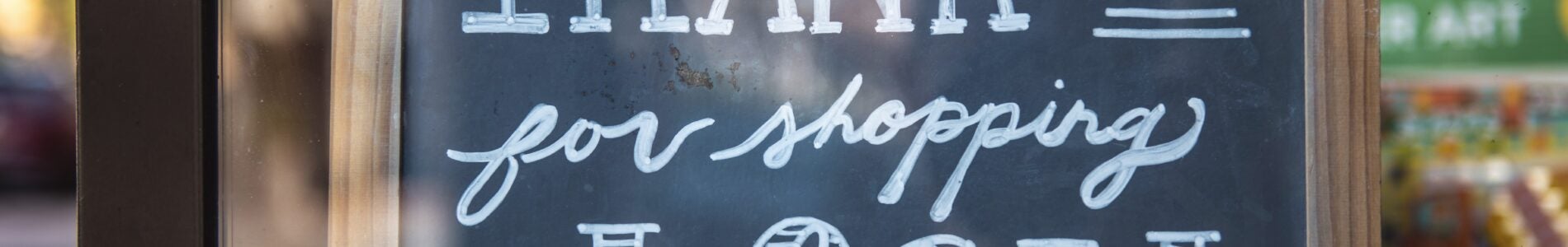 A chalkboard sign with the message "Thank you for shopping local" written in white, set in a wooden frame.
